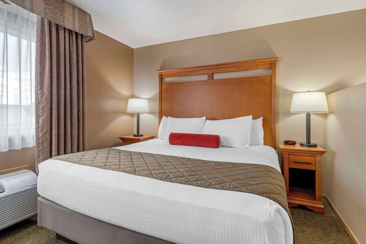 A hotel room with a large bed, two bedside tables with lamps, a heater, and a window with curtains.