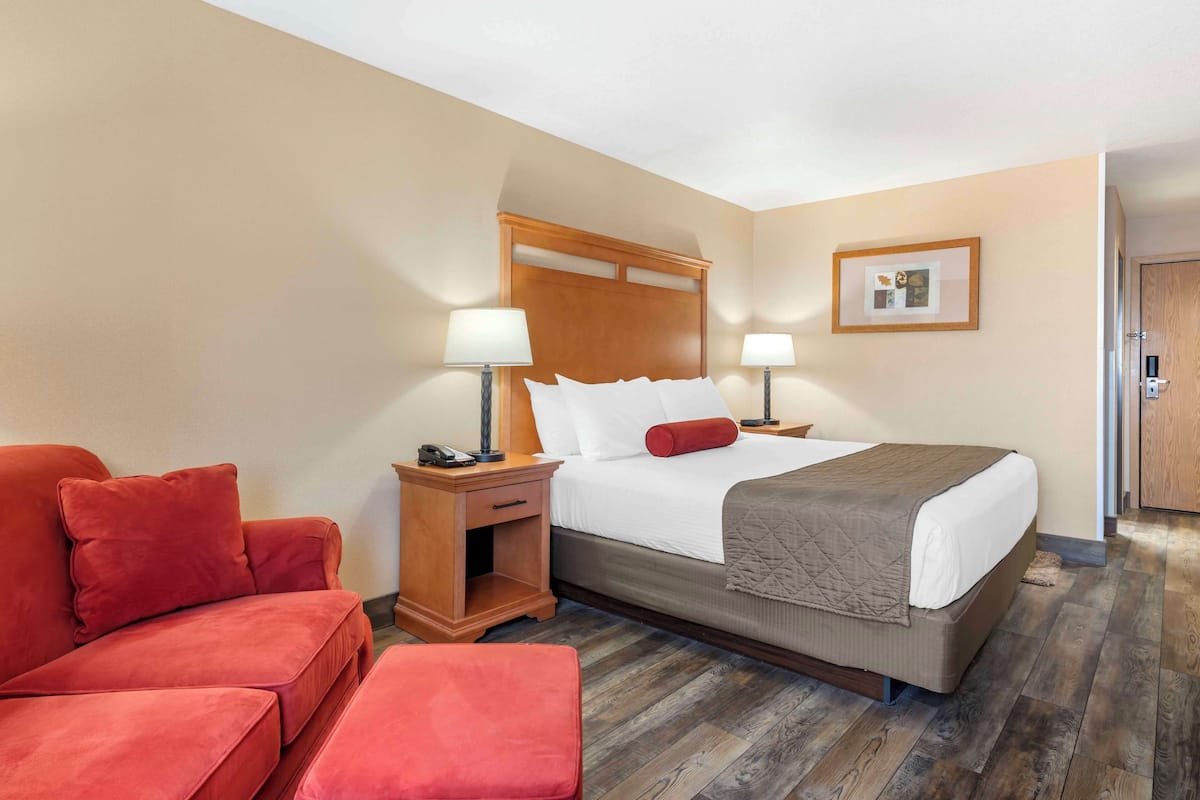 A hotel room with a bed, two bedside tables with lamps, a red sofa, and a wooden floor.