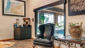 Une pièce avec un fauteuil en cuir, une table basse en verre, un panier en osier, une carte accrochée au mur et un sol carrelé imitant un motif de briques.