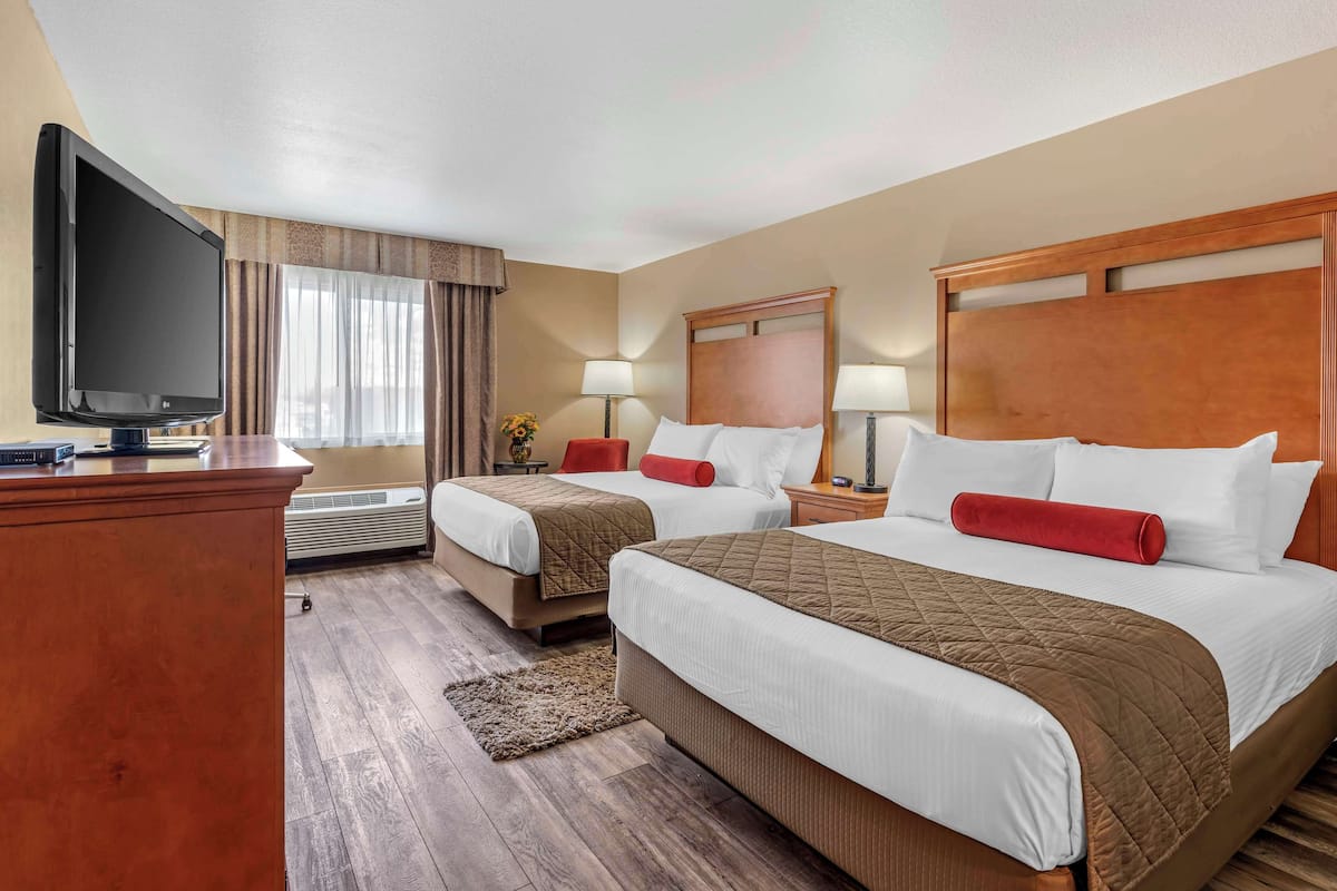 A hotel room with two beds, a TV, a desk, and a window with curtains.