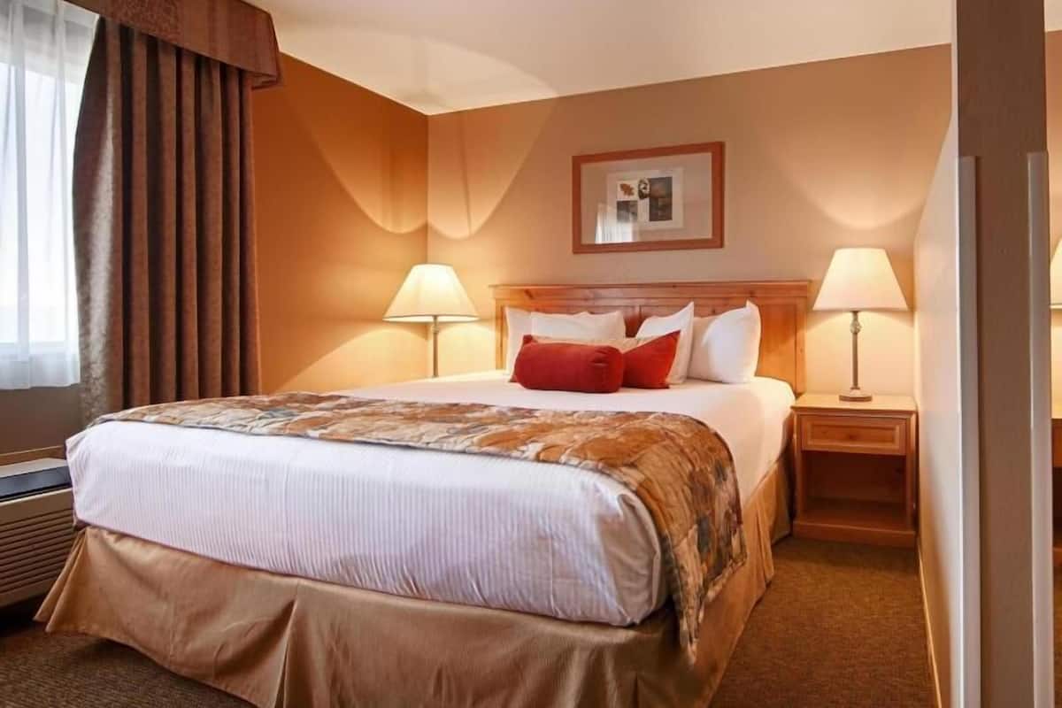 A hotel room with a bed, two bedside tables with lamps, a framed picture on the wall, and a window with curtains.