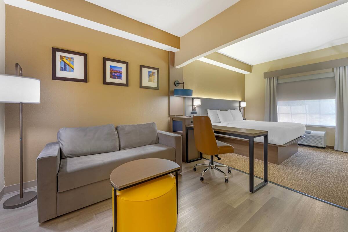 A hotel room with a sofa, a desk, a chair, a bed, a nightstand, and framed pictures on the wall.