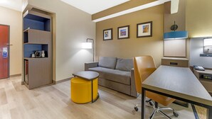 Habitació d'hotel amb sofà, una taula petita, escriptori, làmpada, màquina de cafè i armari.