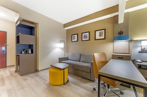 A hotel room with a sofa, a small table, a desk, a lamp, a coffee machine, and a wardrobe.