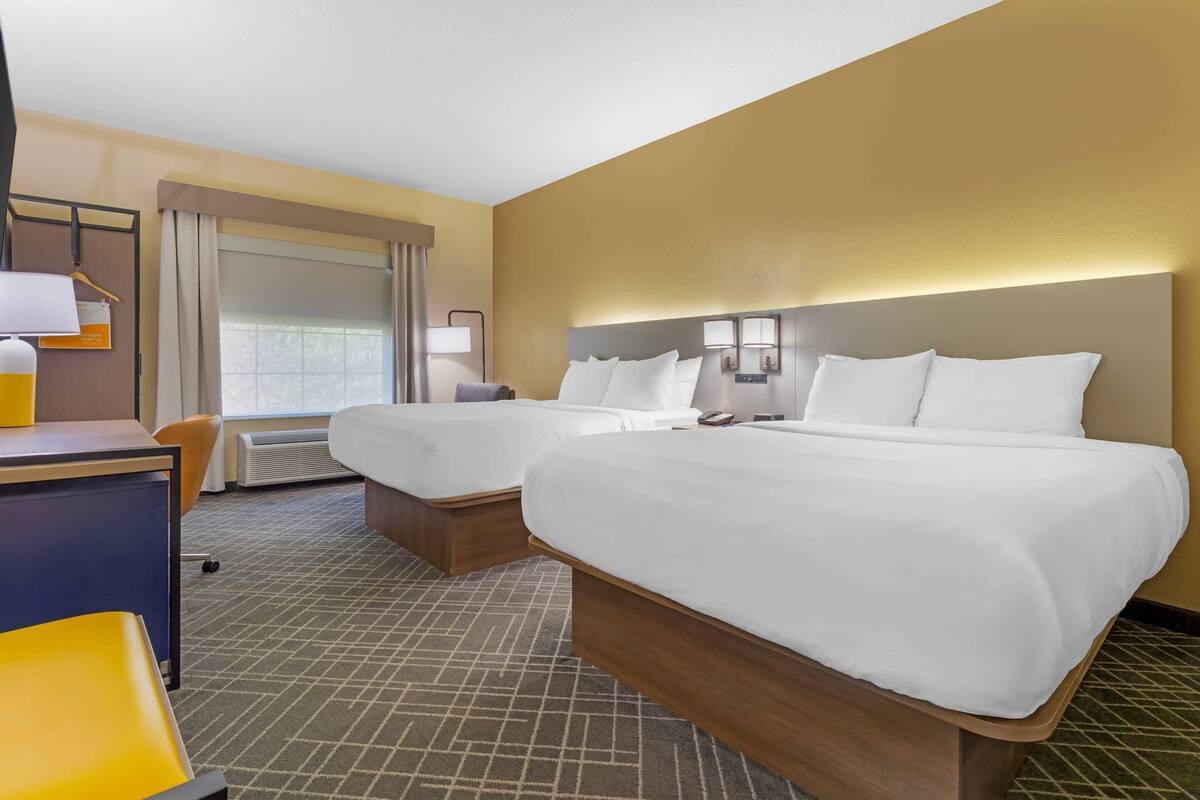 A hotel room with two beds, a desk, a chair, and a window with curtains.
