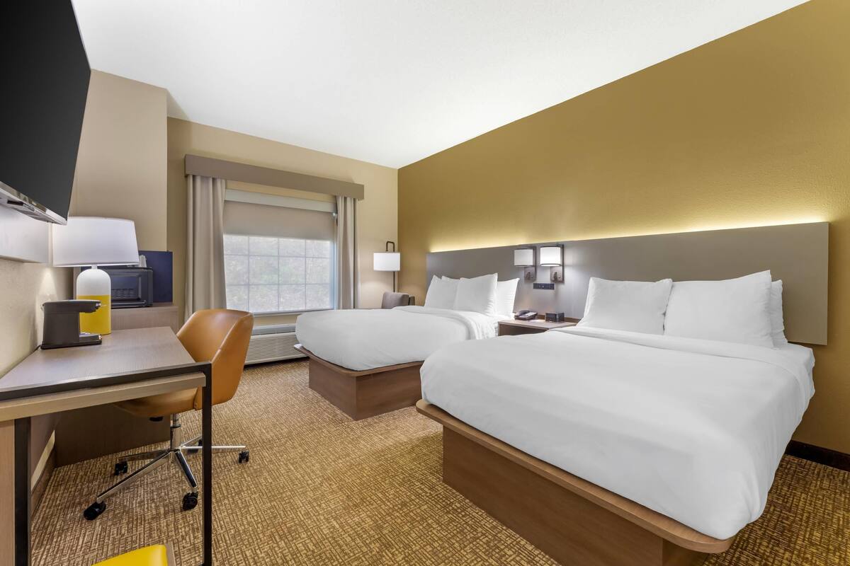 A hotel room with two beds, a desk, a chair, a TV, and a window.