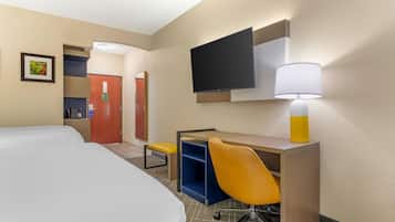 A hotel room with a bed, desk, chair, TV, and lamp.