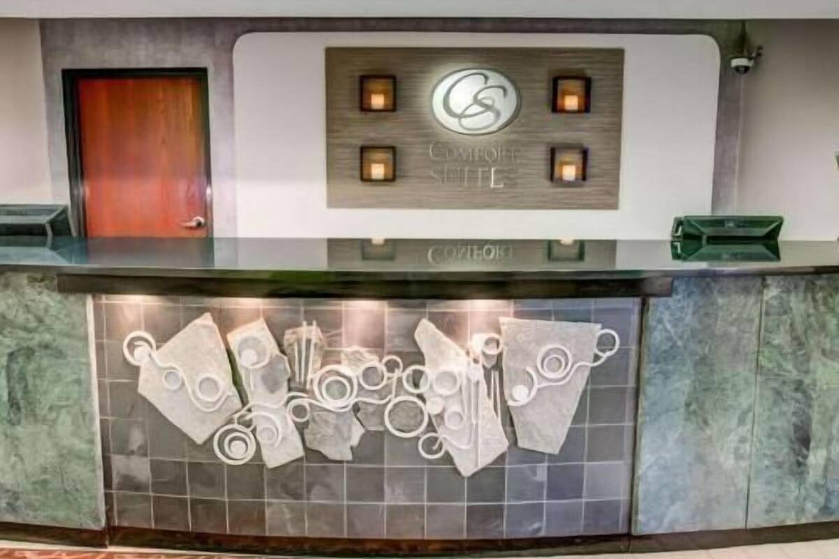 A reception desk with a logo, a wooden panel with the text 'Comfort Suite,' and a green trash bin.