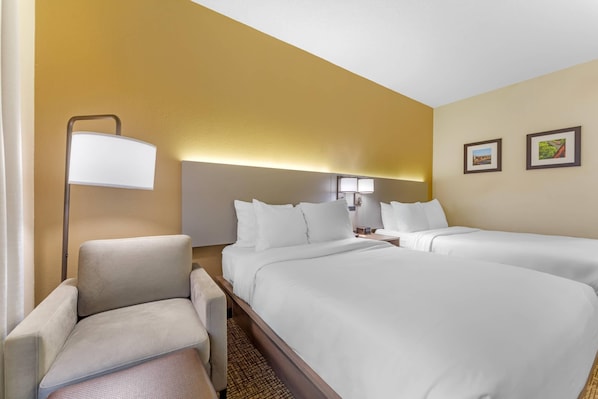 Une chambre d’hôtel avec deux lits, une chaise, une lampe et deux tableaux encadrés au mur.