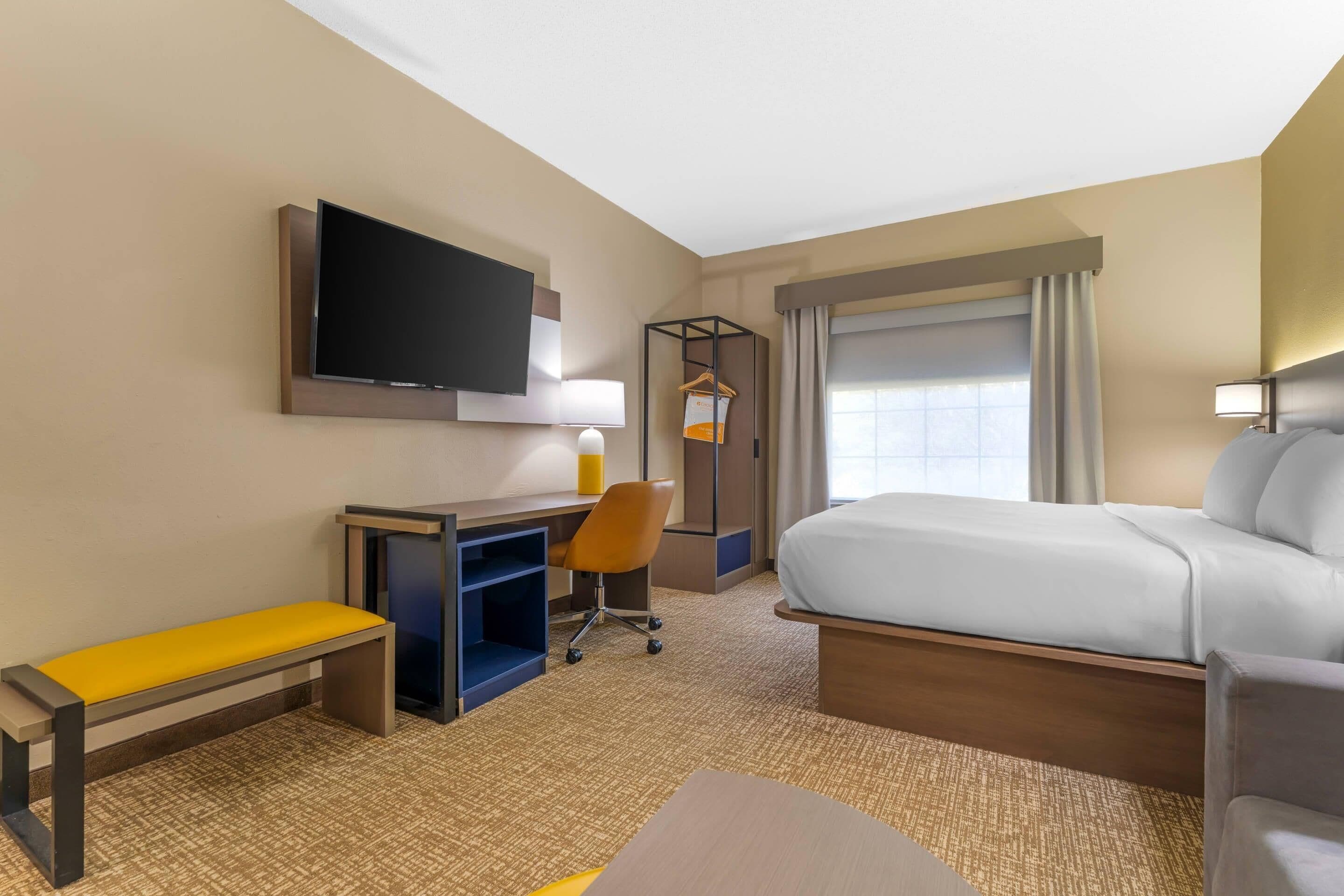 A hotel room with a bed, desk, chair, TV, and window.