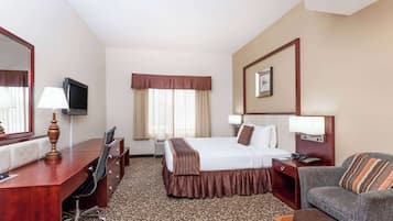 A hotel room with a bed, a desk, a chair, a TV, a lamp, a picture on the wall, and a patterned carpet.