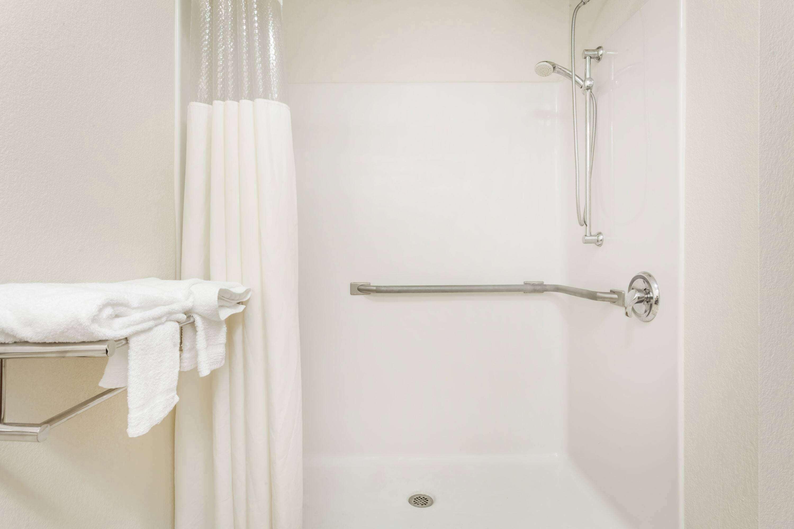 Une douche blanche équipée d’une barre d’appui, d’un porte-serviettes et d’un pommeau de douche.