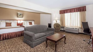 Una habitación de hotel con cama, sofá, una mesita, una silla, lámpara y ventana con cortinas.