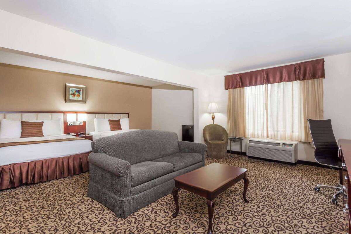 Une chambre d’hôtel avec un lit, un canapé, une petite table, une chaise, une lampe et une fenêtre avec des rideaux.