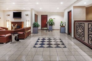 A hotel lobby with a checkered floor, sofas, a fireplace, and potted plants. - Baymont by Wyndham Columbia Fort Jackson (Columbia)