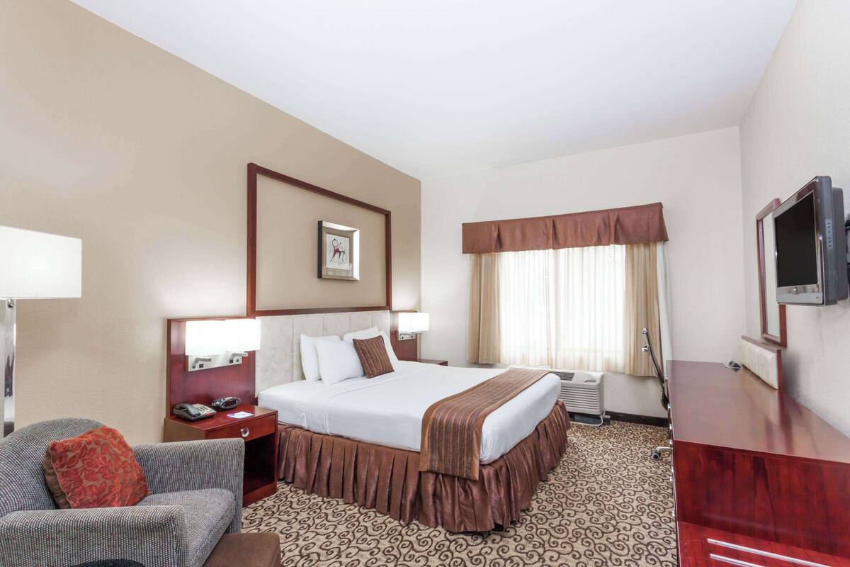 Une chambre d’hôtel avec un grand lit, un bureau, une chaise, une télévision et une fenêtre avec des rideaux.