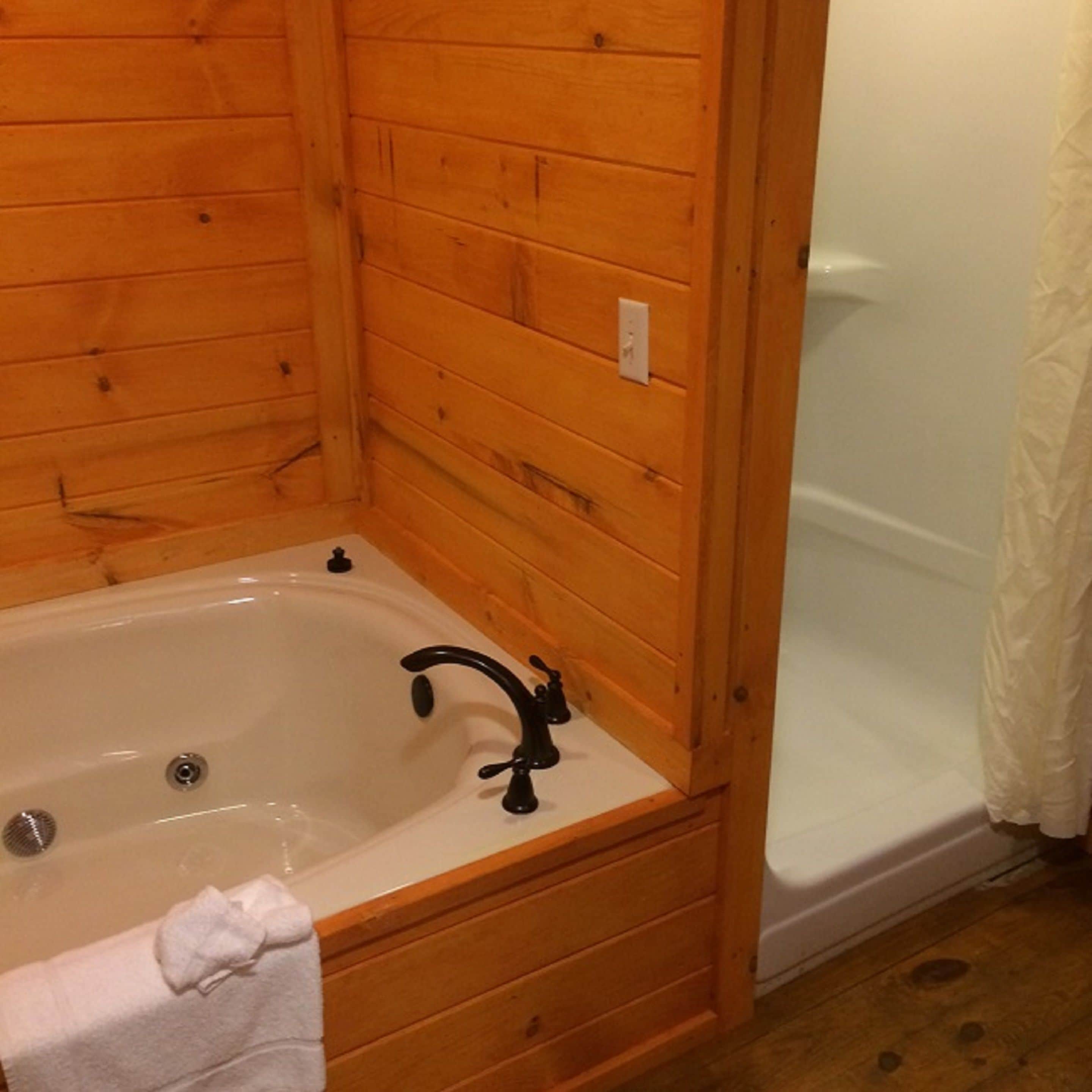 A wooden cabin bathroom with a bathtub, a shower, and a towel on the floor.