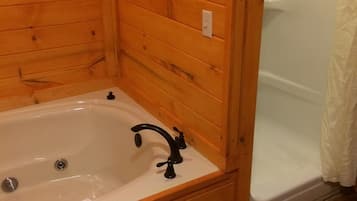 A wooden cabin bathroom with a bathtub, a shower, and a towel on the floor.