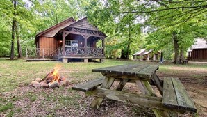 A rustic cabin with a fire pit and picnic table in a wooded area. - The Smokehouse Lodge and Cabins (Monteagle)