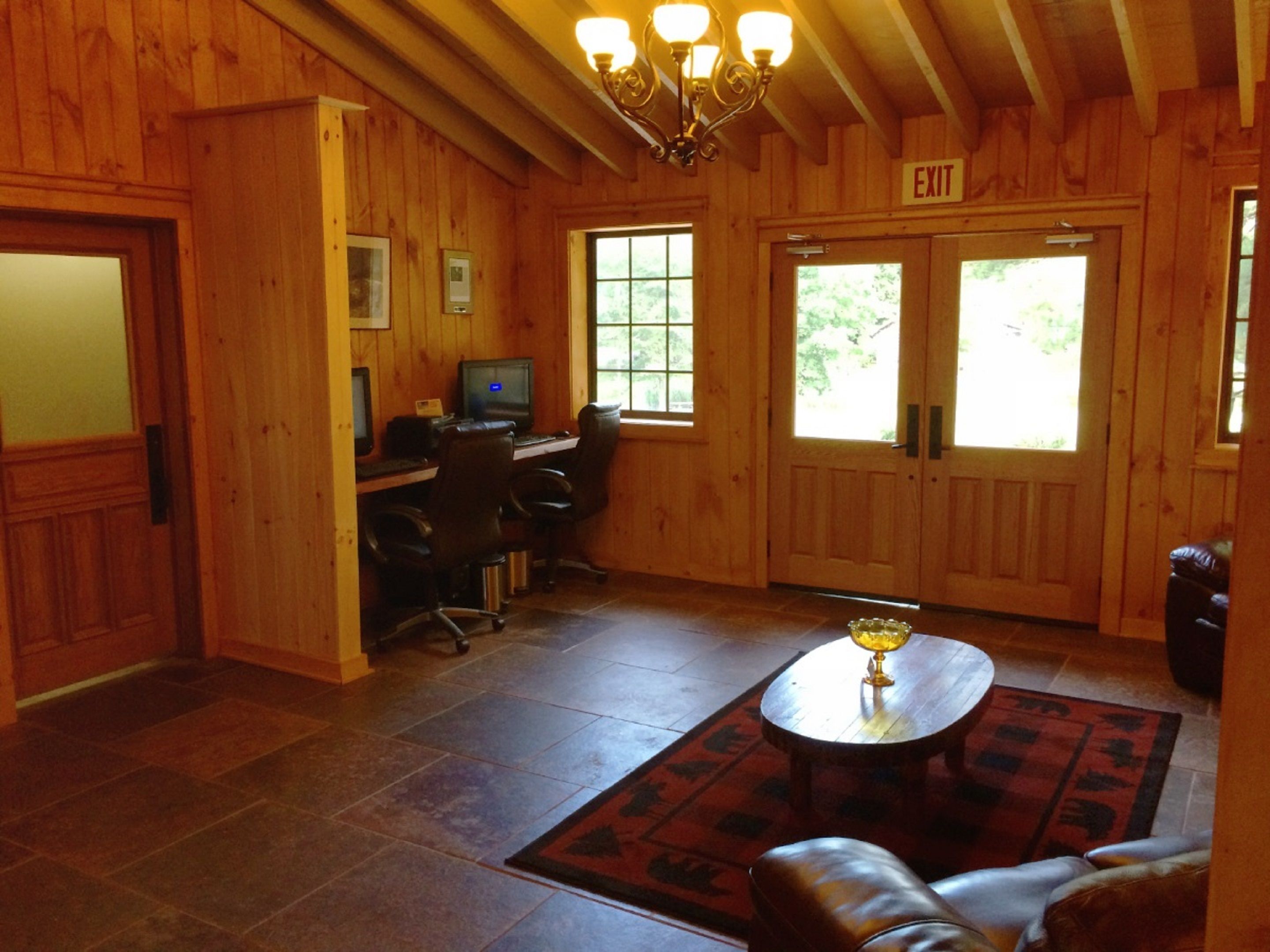 A wooden interior with a computer desk, two chairs, a coffee table, and an exit sign.