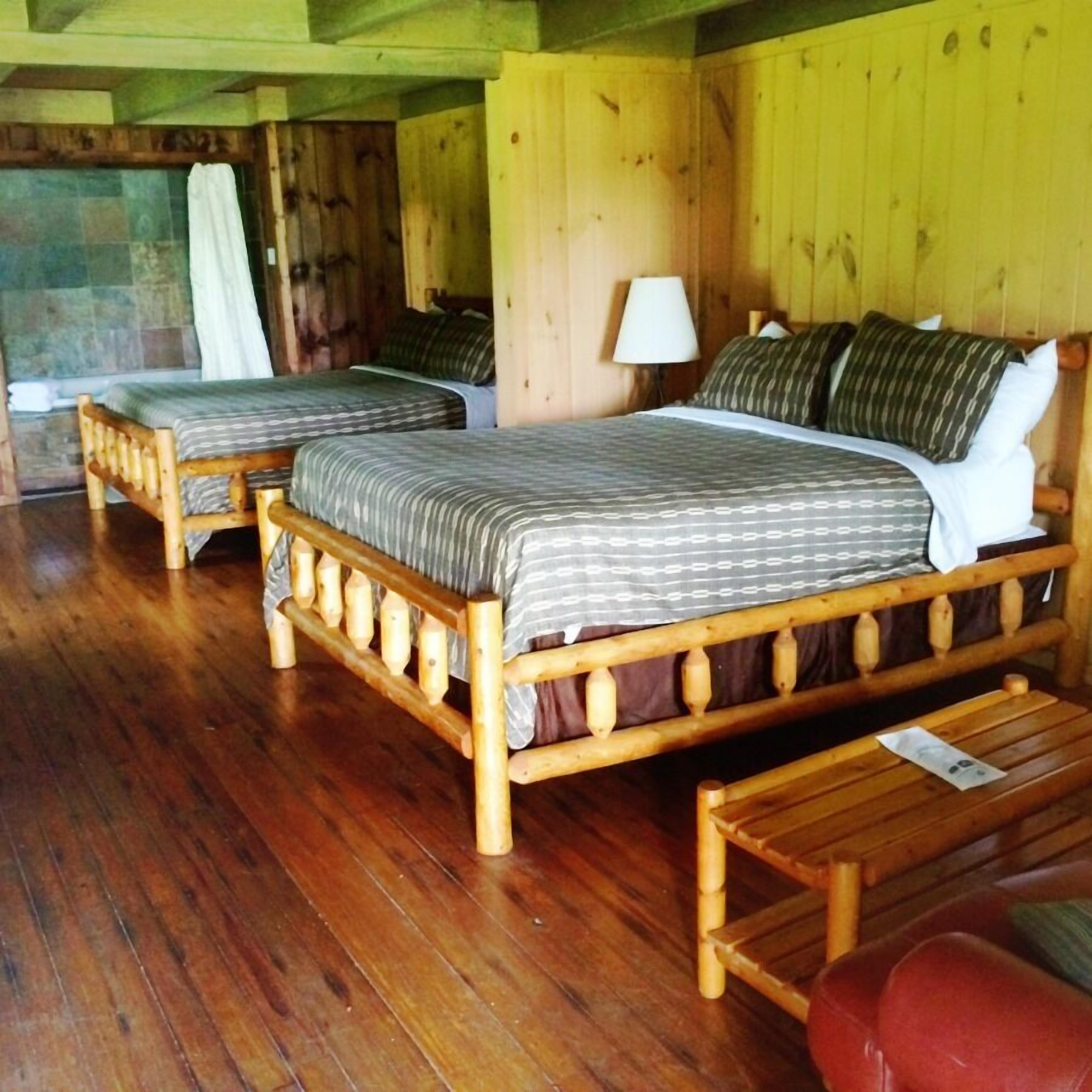 A wooden room with two beds, a wooden bench, and a stone wall.