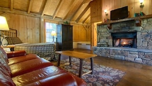 A cozy cabin interior with a stone fireplace, wooden walls, a leather sofa, and a television mounted above the fireplace. - The Smokehouse Lodge and Cabins (Monteagle)
