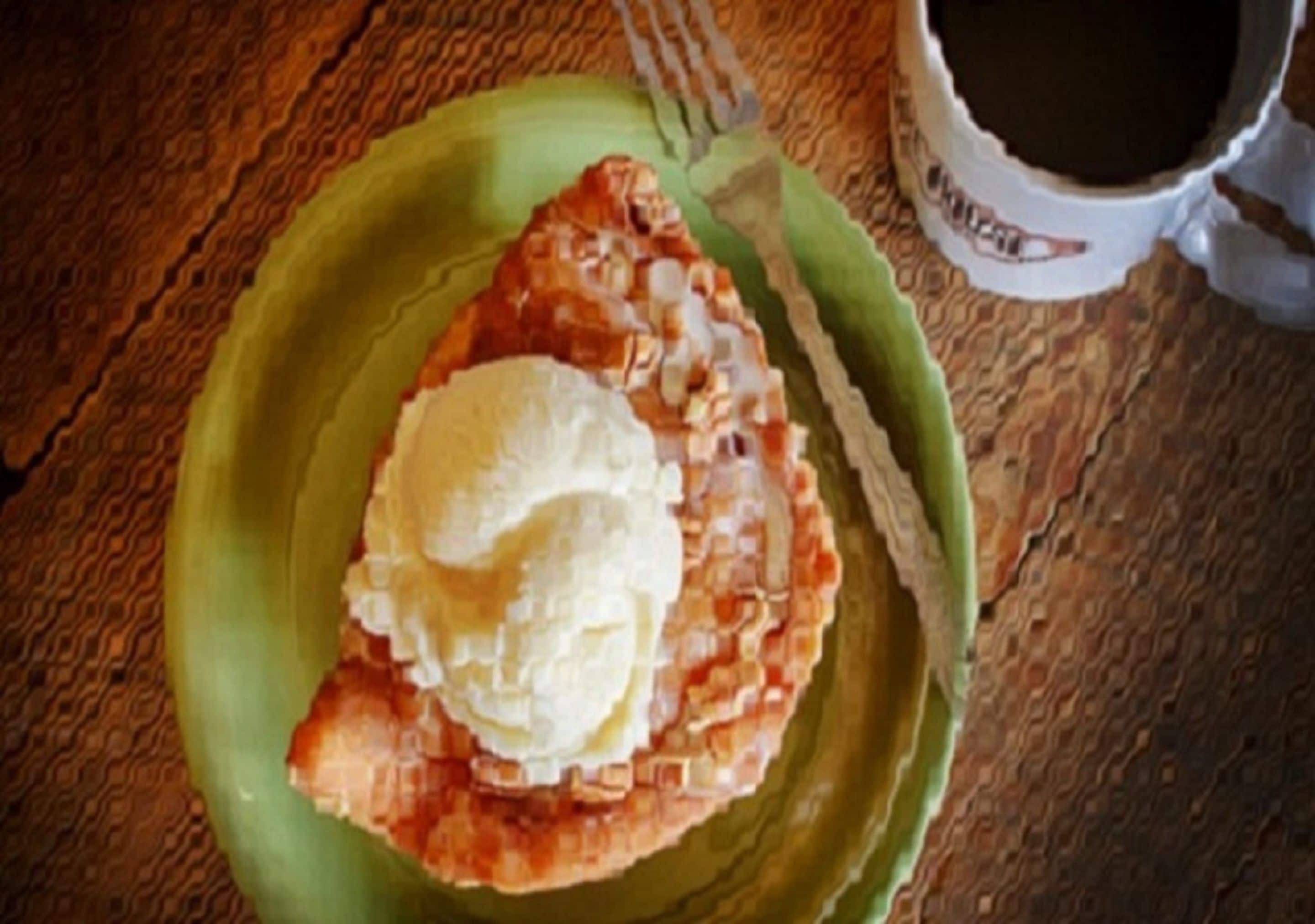 A green plate with a slice of pie and a scoop of ice cream on a wooden table.