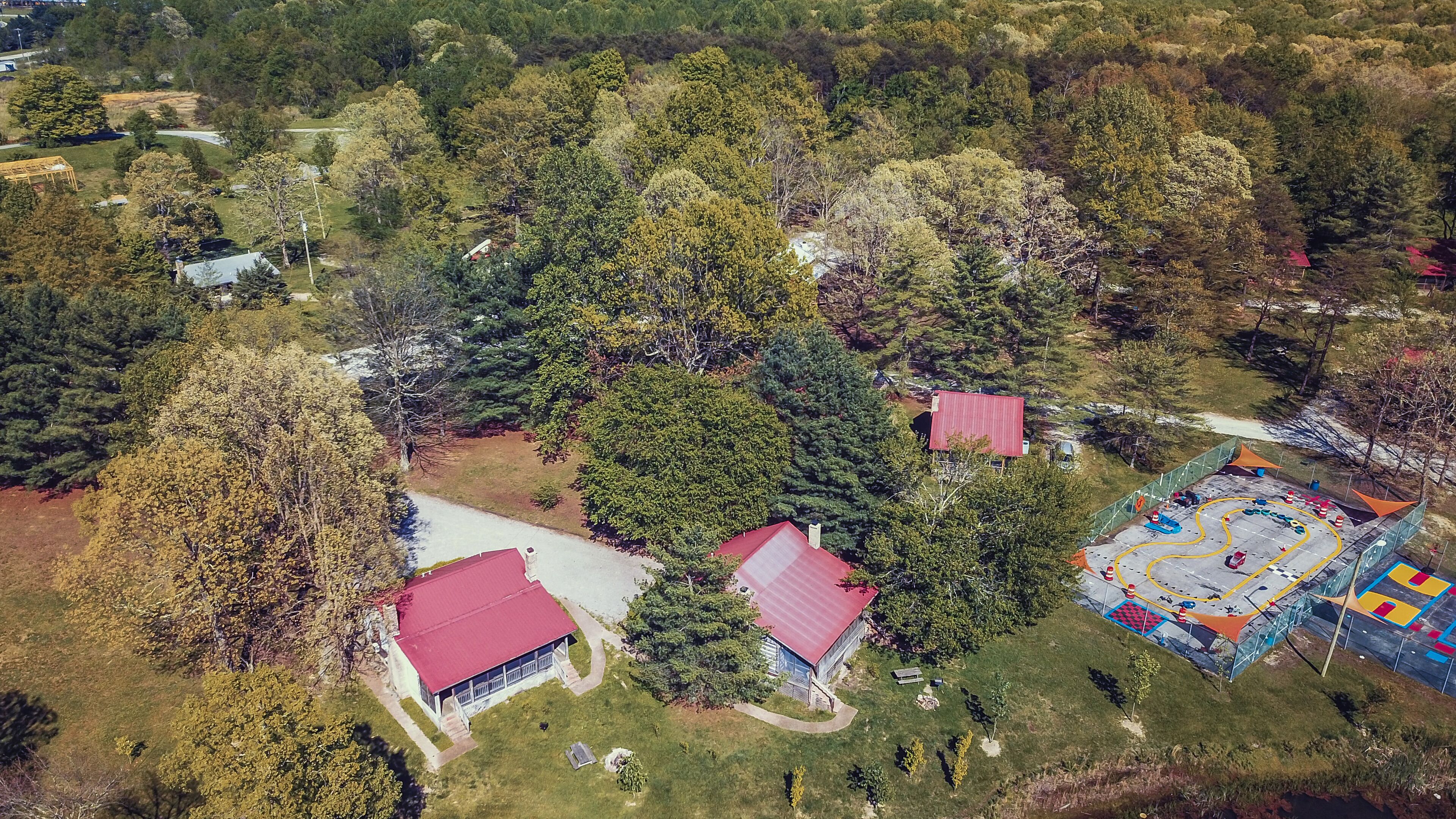 Vista aérea de una propiedad con dos edificios, una zona deportiva cercada y vegetación circundante.