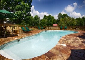 Piscina con cubierta de piedra, rodeada por una valla de madera y sillones de jardín verdes.