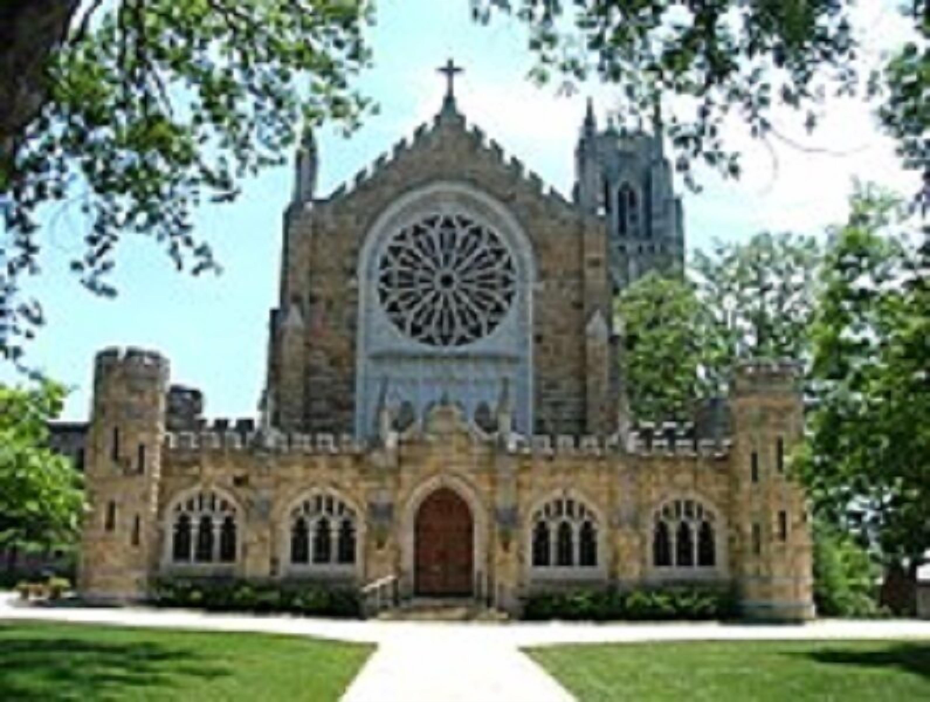 A historic church with a large circular stained glass window, arched doorways, and a tall bell tower.