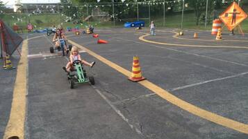 A parking lot with a child riding a tricycle, surrounded by traffic cones and a blue car in the background.