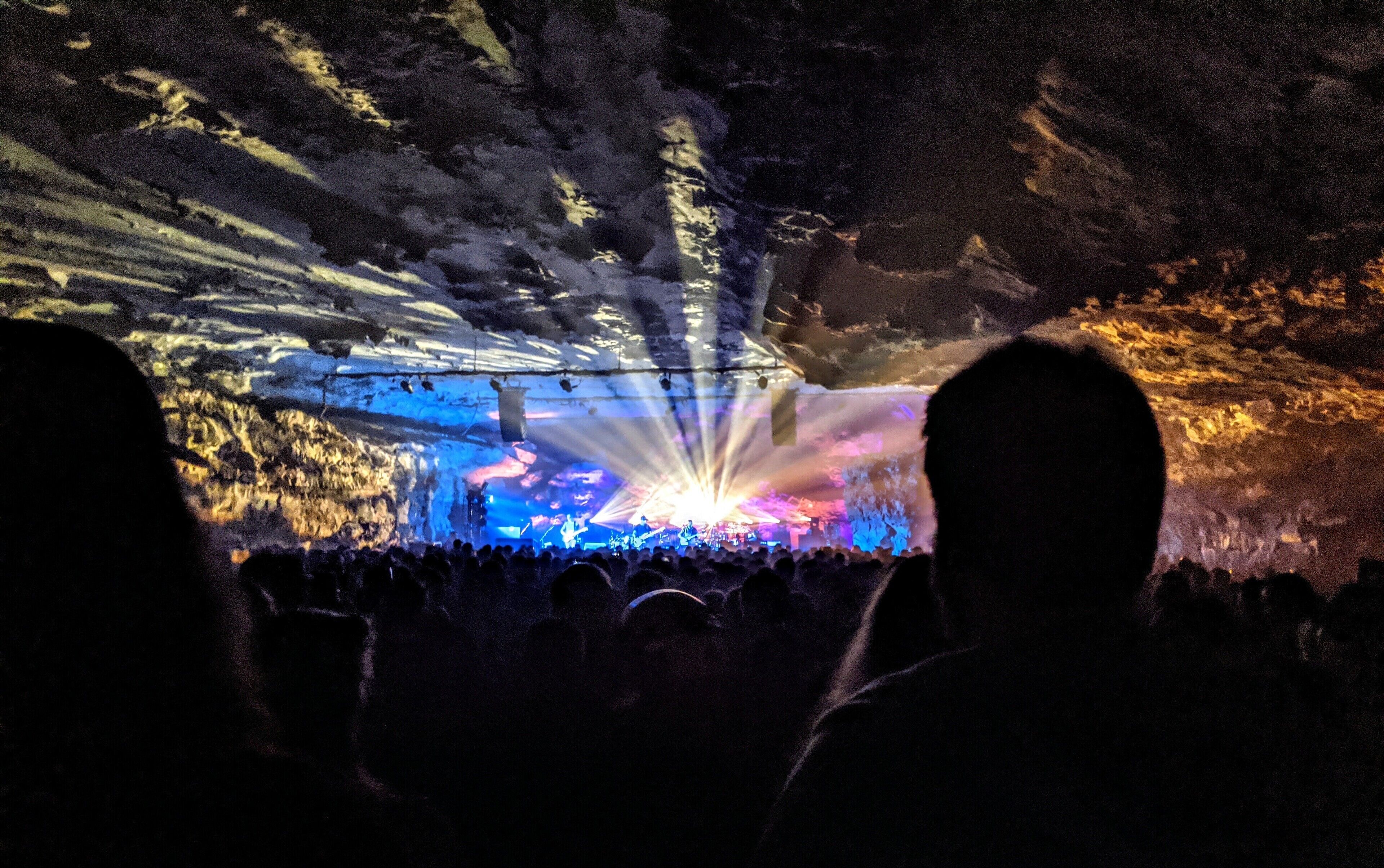 A concert with a stage and audience in a cave-like setting.