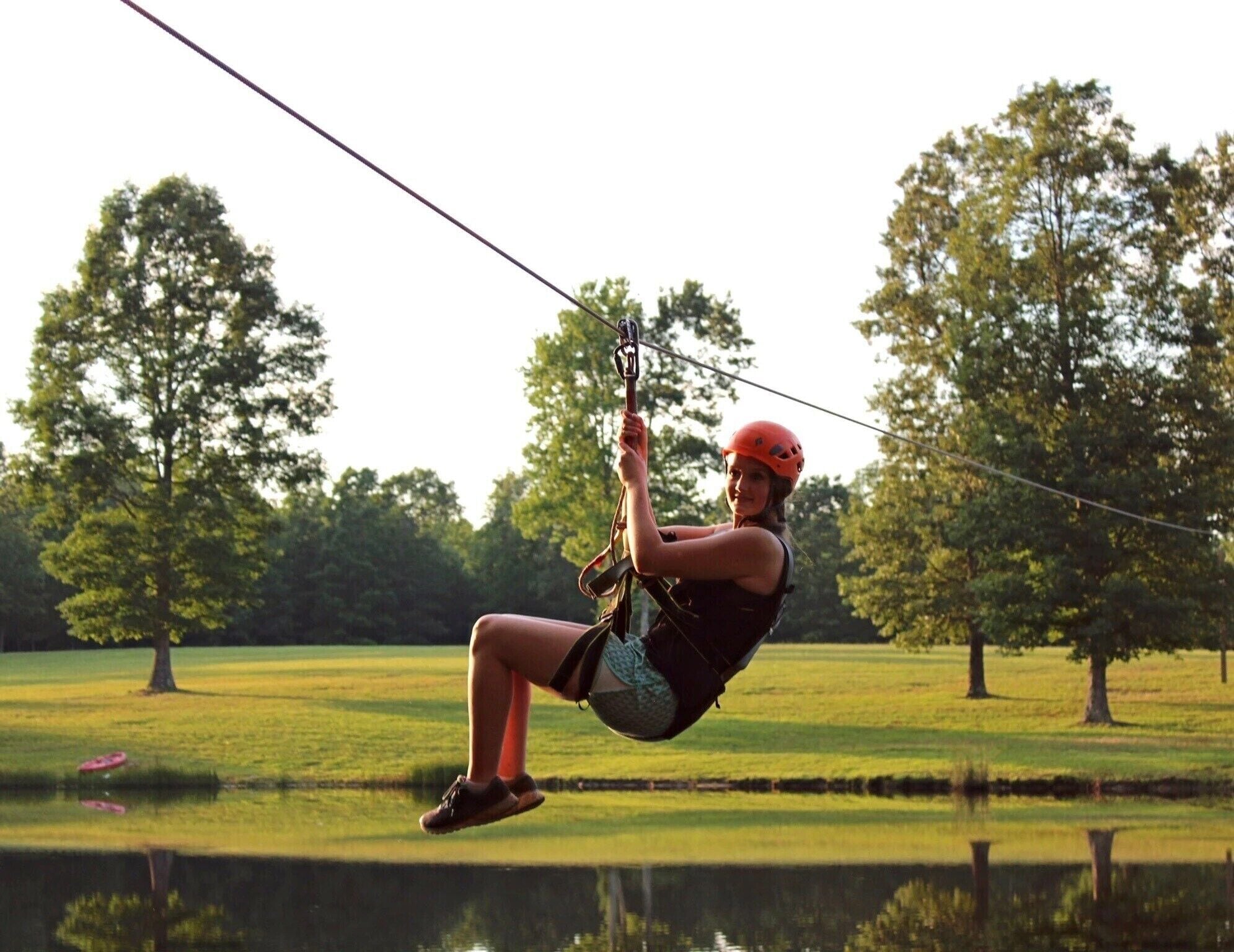 A person ziplining over a body of water with trees in the background.