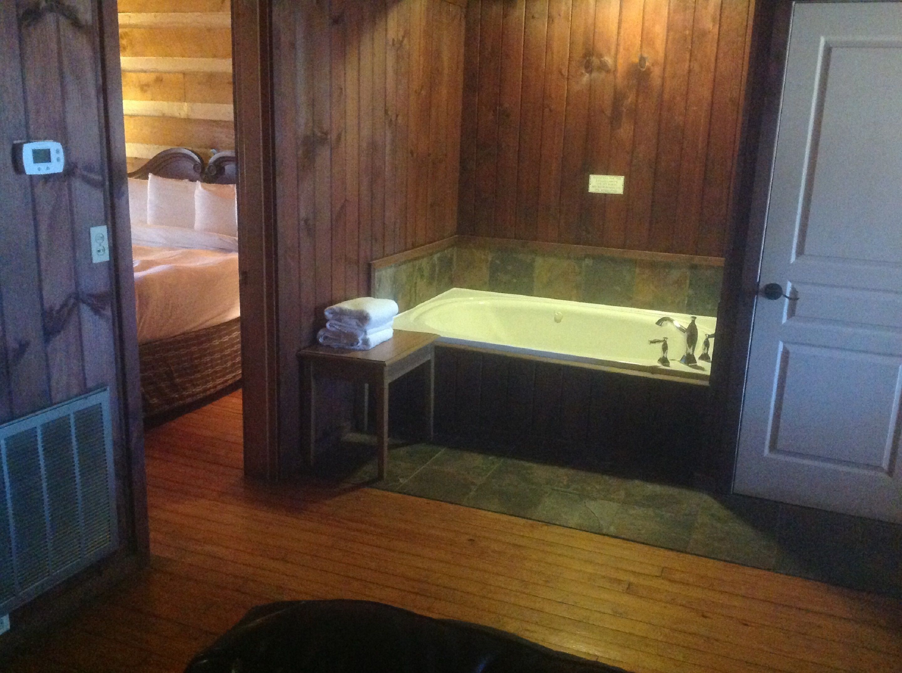 A wooden bathroom with a bathtub, a small table with towels, and a door.
