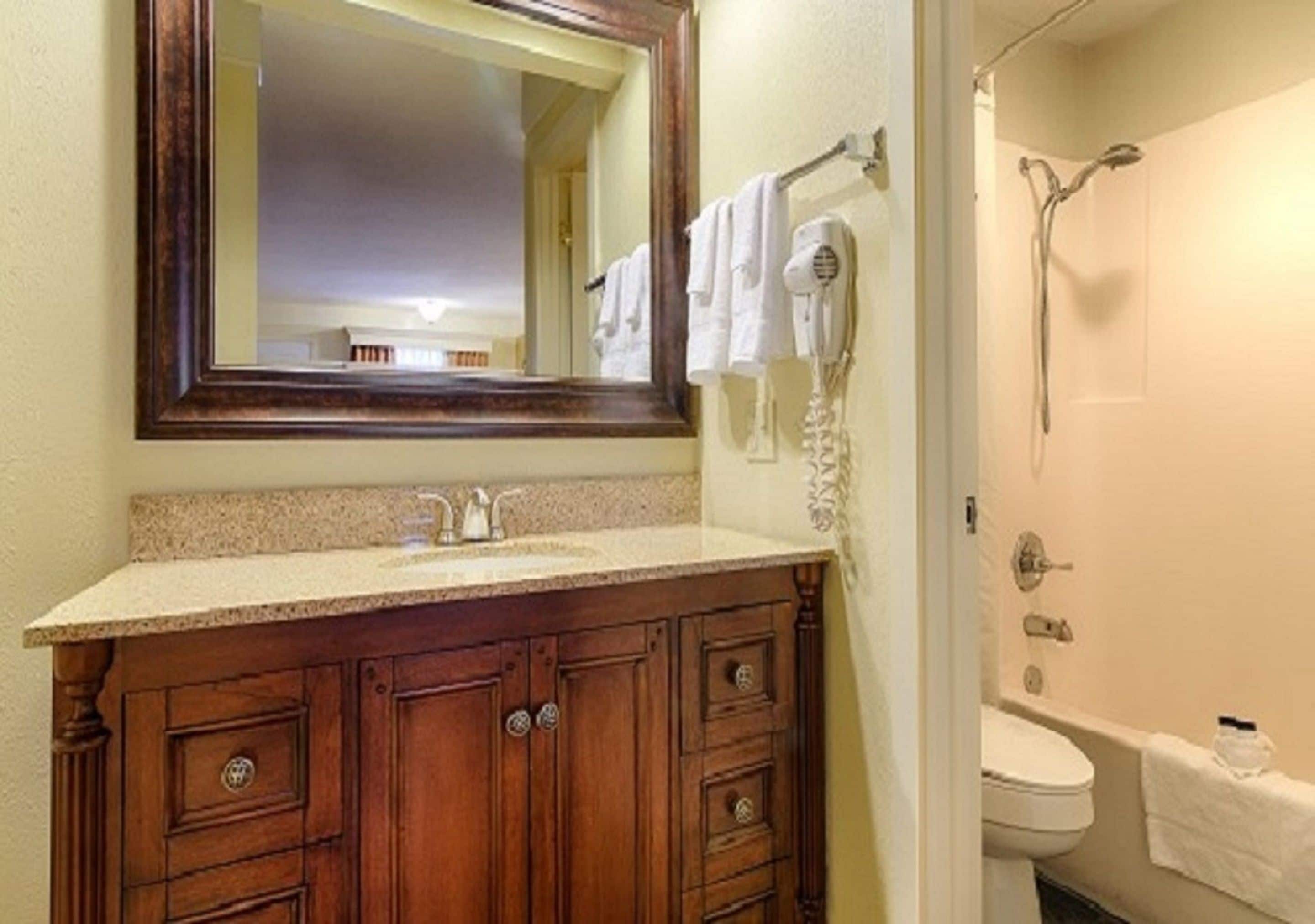 Un baño con tocador de madera, lavamanos, espejo, perchero para toallas y ducha.