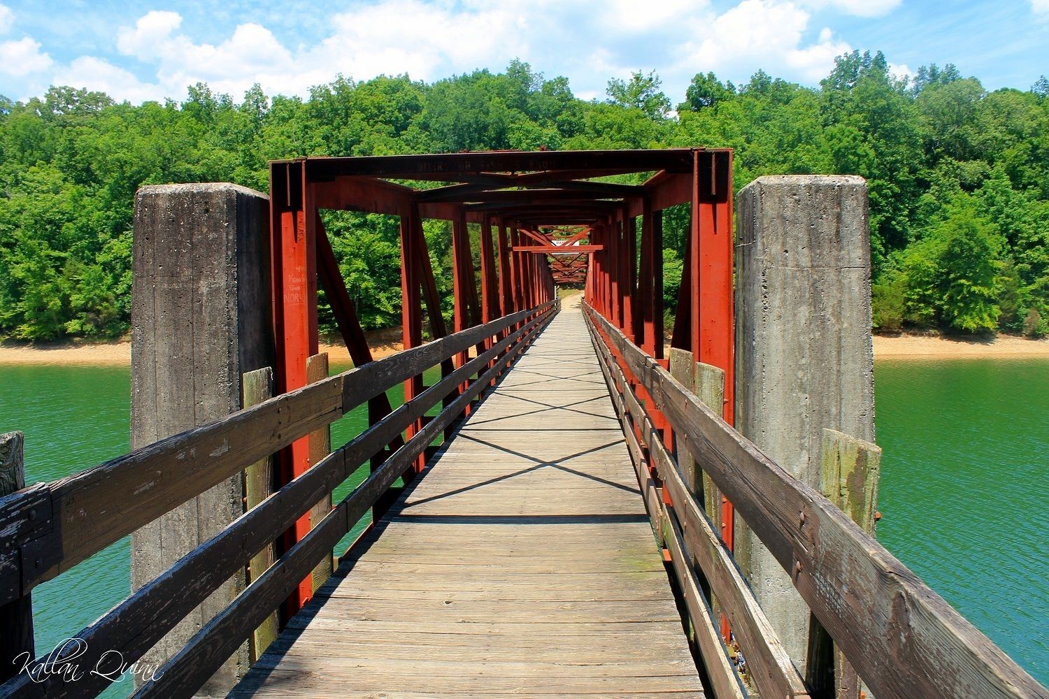 A wooden bridge with red supports and a wooden walkway leading to a forested area.