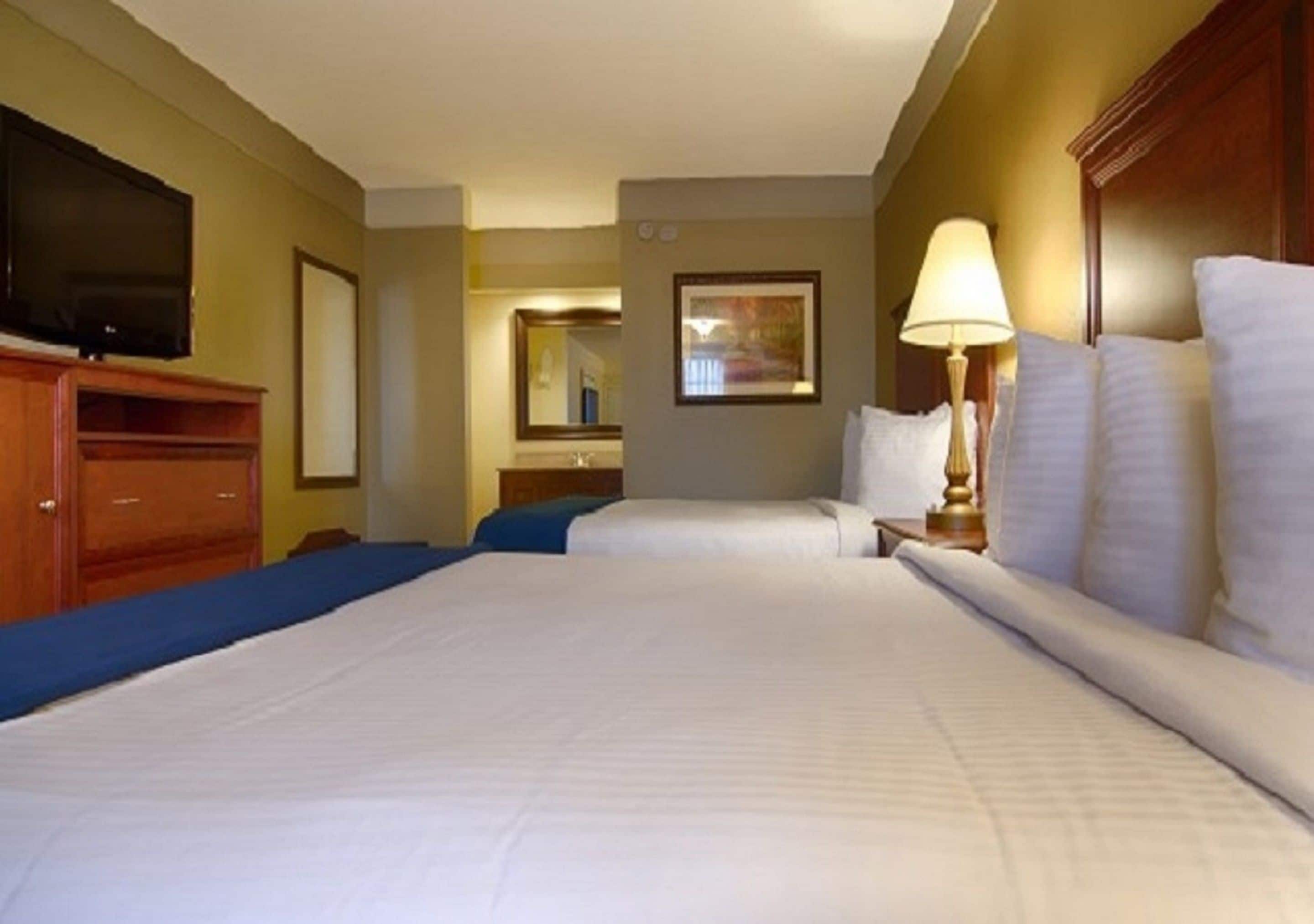 Habitación de hotel con dos camas, un televisor, un espejo y una lámpara.