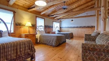 Une pièce rustique avec un plancher en bois, un lit, deux chaises et un bureau avec une lampe.