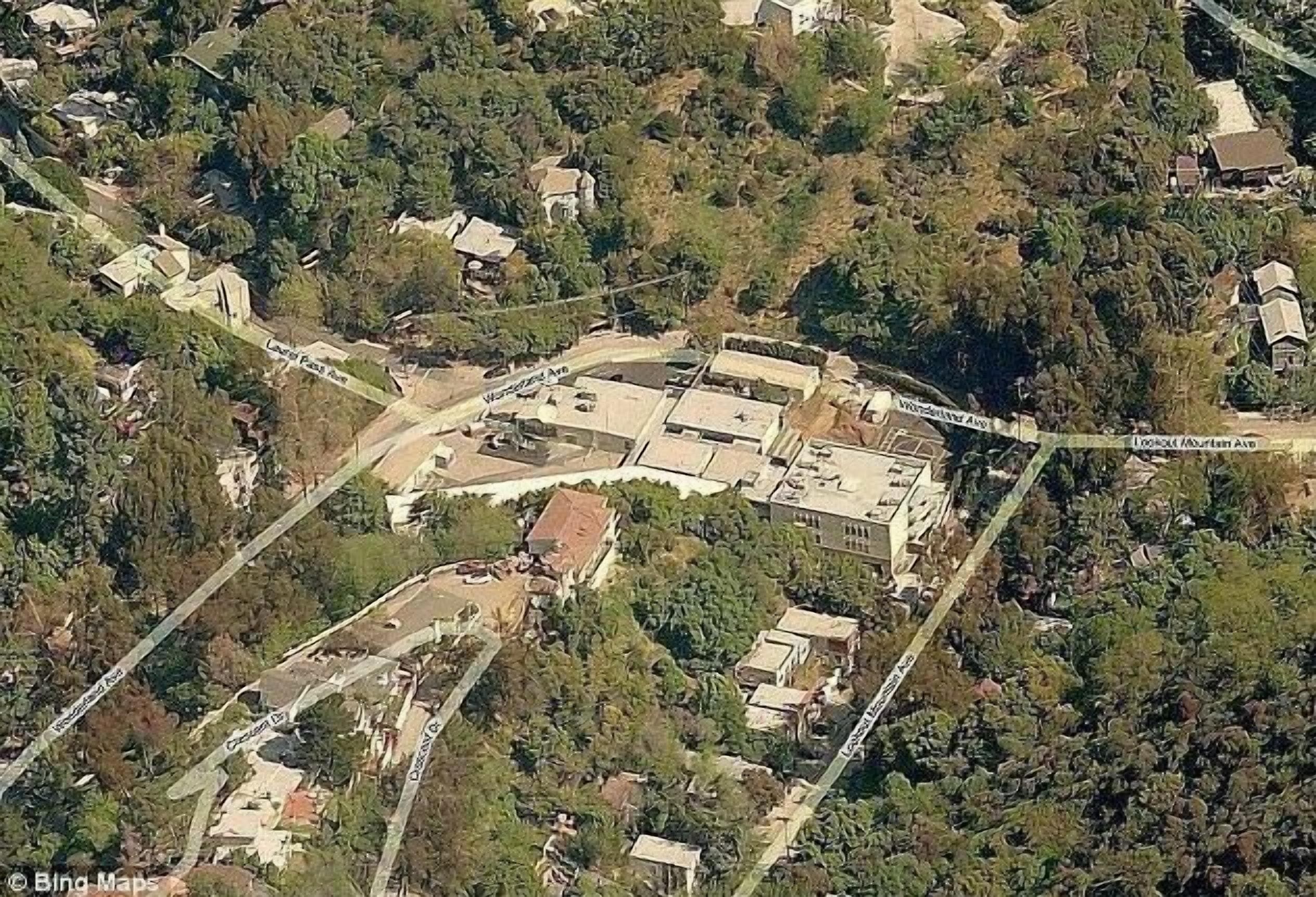 Vista aèria d'una zona residencial amb un gran complex immobiliari envoltat de vegetació densa i cases més petites.