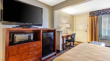 A hotel room with a flat-screen TV, a microwave, a refrigerator, a desk with a chair, and a bed with a patterned bedspread.