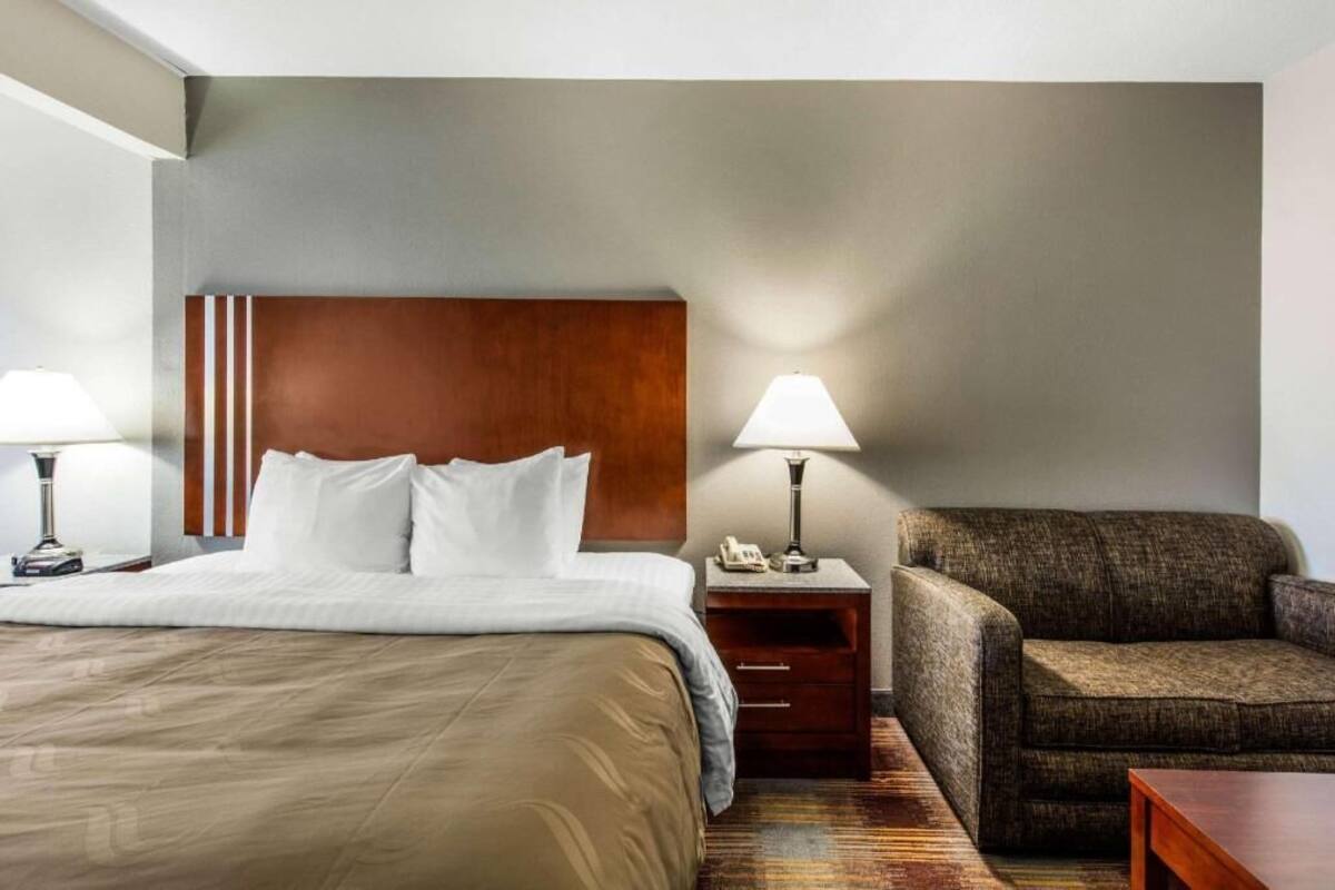 Una habitación de hotel con cama, mesitas de noche, lámpara, sofá y suelo de madera.