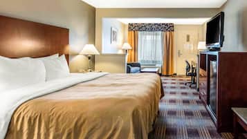 Una habitación de hotel con una cama grande, un escritorio con una silla, un televisor y una lámpara de escritorio.