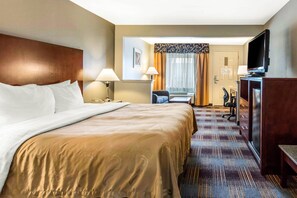 A hotel room with a large bed, a desk with a chair, a television, and a desk lamp. - Quality Inn Memphis Airport (Memphis)