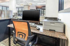 A hotel office with a desk, computer, printer, and a chair.