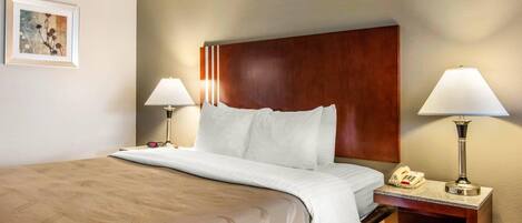 A hotel room with a bed, two bedside lamps, a nightstand with a phone, and a framed picture on the wall.