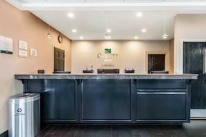 A hotel reception desk with a 'Quality Inn' sign above, a clock, and a recycling bin.