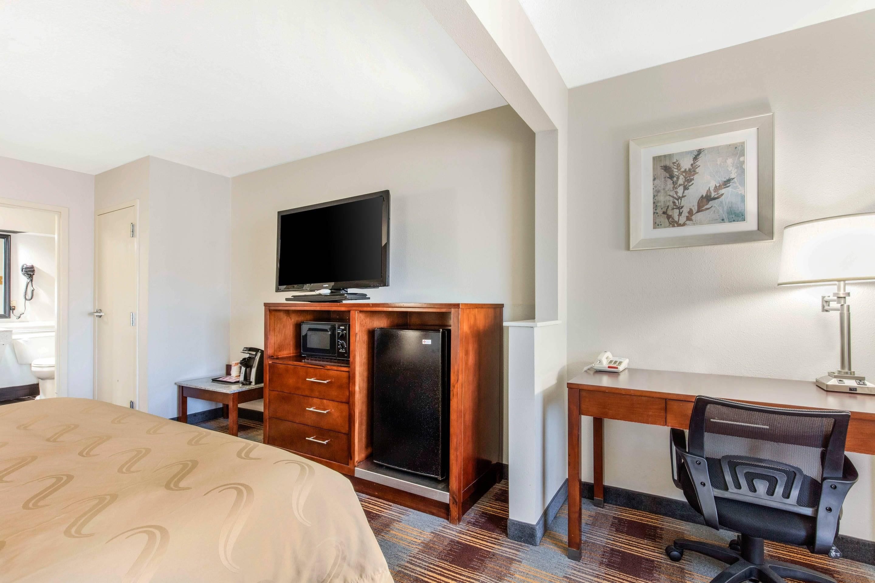 Habitación de hotel con una cama, un escritorio con una silla, televisor, refrigerador, microondas y teléfono.