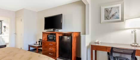 A hotel room with a bed, a desk with a chair, a television, a refrigerator, a microwave, and a telephone.