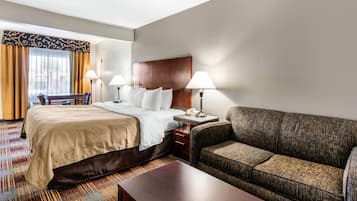 Una habitación de hotel con una cama, un sofá, un escritorio con lámpara y un teléfono.