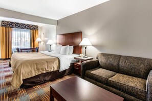 A hotel room with a bed, a sofa, a desk with a lamp, and a telephone. - Quality Inn Memphis Airport (Memphis)